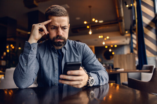 An Upset Man Is Sitting In Cafe And Looking At The Phone.