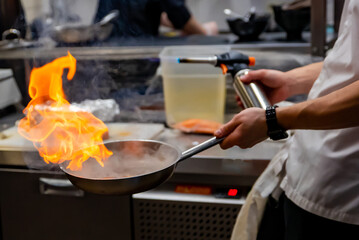 Chef hand in restaurant kitchen with pan, cooking flambe on food