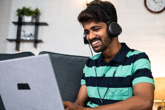 Happy smiling young man with headphone laughing while wathing comedy movie on laptop - concept of leisure activities, relaxation and selfcare