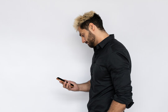 Concentrated businessman reading news on his smartphone. Male Caucasian model with brown eyes, ombre painted hair and beard in black shirt reading important information. Modern technology concept