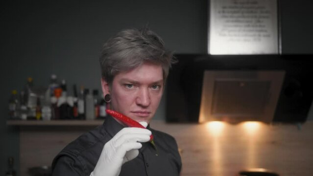 Attractive professional male chef in an elegant black shirt with an alternative look (tattoos, colored hair) biting off a red chili, looking into camera 
A modern, fancy looking kitchen, Slow Motion