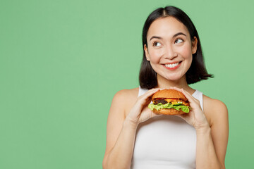 Young happy woman wear white clothes hold eat burger look aside on workspace area mockup isolated on plain pastel light green background. Proper nutrition healthy fast food unhealthy choice concept.