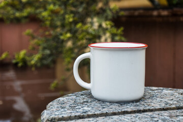 Obraz na płótnie Canvas Enamel mug standing on the top of a marble fence while showing out of focus plant behind it