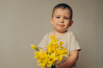 portrait of a smiling child 2-3 years old with a bouquet of yellow daffodils in his hands