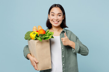 Fototapeta na wymiar Young happy woman wears casual clothes hold brown paper bag with food products show thumb up gesture isolated on plain blue cyan background studio portrait. Delivery service from shop or restaurant.