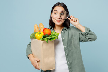 Fototapeta na wymiar Young fun woman wearing casual clothes hold brown paper bag with food products look through magnifier isolated on plain blue cyan background studio portrait. Delivery service from shop or restaurant.