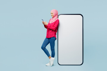 Full body young arabian muslim woman wear pink abaya hijab near big huge blank screen area use...