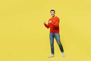 Fototapeta premium Full body profile young fun caucasian happy cheerful man wear orange casual clothes walking going do winner gesture isolated on plain yellow color background studio portrait. People lifestyle concept.
