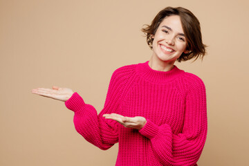 Young smiling woman wears pink sweater point hands arms aside indicate on workspace area copy space...