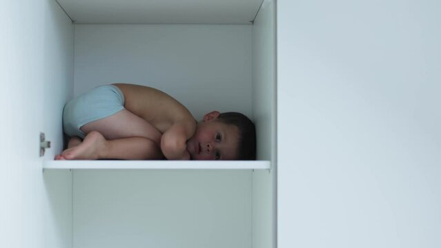 Scared Child Boy Hides Inside Closet, Little Kid Frightened Curling Up On Shelf Inside White Furniture. Children Safety Concept. Family Problems Parents And Children Communication Abuse Kids. Personal