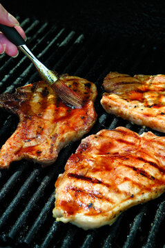 Cropped hand of woman applying sauce on meat over barbecue grill