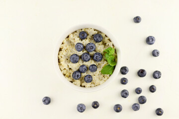 Oats porridge bowl. Morning healthy breakfast oatmeal cereals with blueberries, mint leaves on white