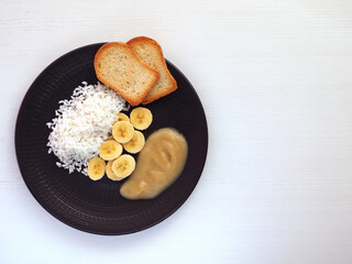 Banana, rice, applesauce and toast on a dark plate. Copy space