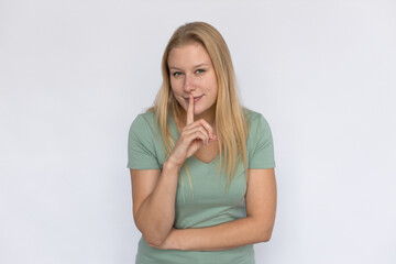 Playful woman showing hush gesture. Young female model holding finger at lips. Portrait, studio shot, secret, silence concept