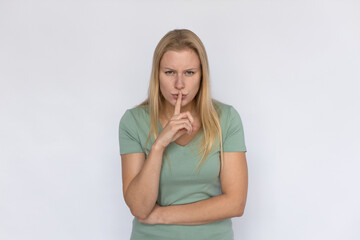 Angry woman with finger at lips. Young female model showing hush gesture. Portrait, studio shot, secret, silence concept