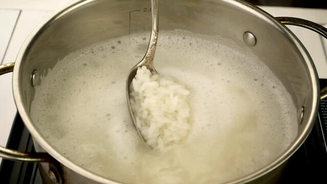 Boiling round rice in metal pot is stirred.