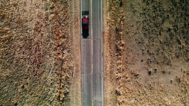 Aerial top down view of a black car on a highway in the middle of the desert in the United States.