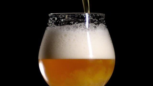 Slow Motion Close up of craft Beer being poured in to a tulip glass, black background