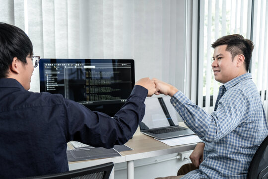 Team of two professional programmers working on website projects in software development and making a fist-bump after mission complete making coding and typing data code password security in office