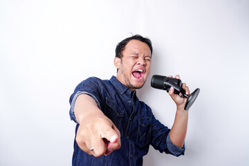 Portrait of carefree Asian man, having fun karaoke, singing in microphone while standing over white background