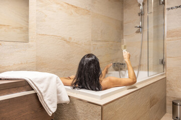 A beautiful brunette enjoys an evening alone in the bathtub with a glass of champagne