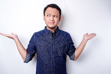 A portrait of an Asian man wearing a blue shirt looks so confused between choices, isolated by a...