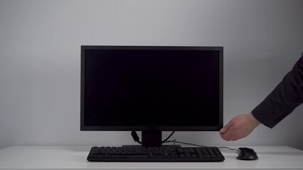 Turning on the monitor with a green screen. A man with his hand turns on the computer screen on the desktop in the office. Chroma key.