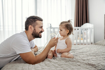 A happy father is cleaning his baby's nose with pump in a bedroom.