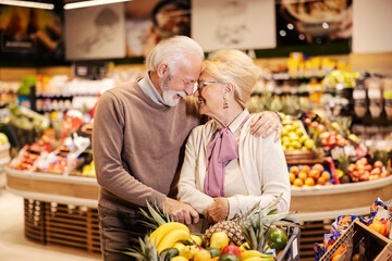 A happy senior couple in love is hugging at the supermarket while shopping.