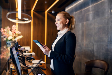 A happy receptionist is talking with hotel guest and making a reservation on a tablet. - obrazy, fototapety, plakaty