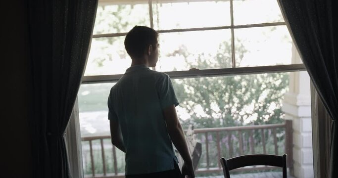 Young man, teenage boy watches out window.