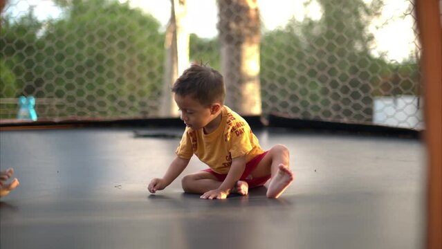 Slow motion of a cute latin baby boy sitting on a trampoline jumping and playing with his mother