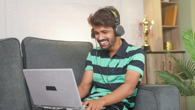 Happy smiing young man with headphone laughing while wathing comedy movie on laptop - concept of leisure activities, relaxation and selfcare