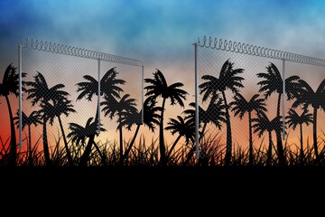 Naklejka premium Barbed wire over silhouette of palm trees against sunset sky