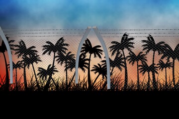 Fototapeta premium Barbed wire over silhouette of palm trees against sunset sky