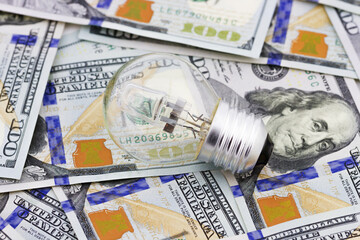 Energy saving concept. Electric light bulb on dollar bills background