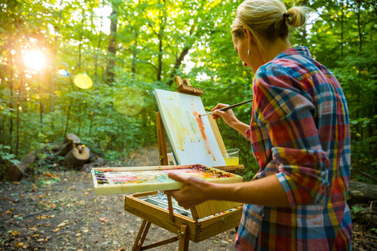 Female painter painting on easel with watercolors in forest at dusk, Neenah, Wisconsin, USA