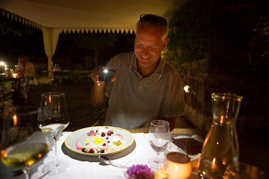 Man shining light on his dessert at outside diner in dark evening with his smartphone, Radovljica, Slovenia
