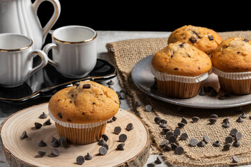 Muffin or cupcake with chocolate chips on wooden table background. Concept of making industrial or homemade pastries.