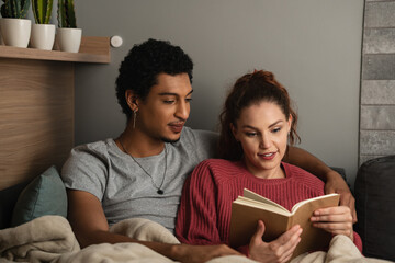 Young couple read book together on sofa in living room at home