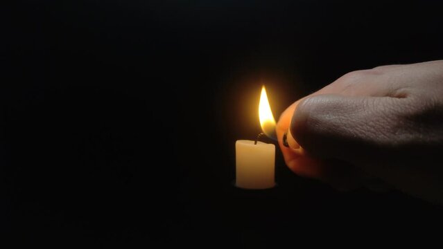 A man ignites a fire with a lighter on candles isolated on a black background