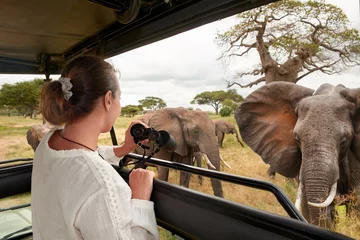 Foto auf Acrylglas Lachsfarbe Woman tourist on safari in Africa, traveling by car with an open roof in Kenya and Tanzania, watching elephants in the savannah