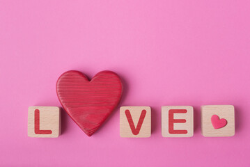 Word Love made of wooden blocks and decorative valentines heart. Pink background with copy space. Valentine’s day conceptual greeting