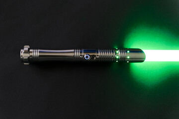 Colorful green glowing laser sword with shiny silver metal grip against black background. Photo...