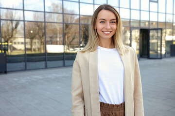 Fototapeta premium Portrait of the beautiful smiling businesswoman in formal outfit standing near the business centre looking at the camera. People and business concept.