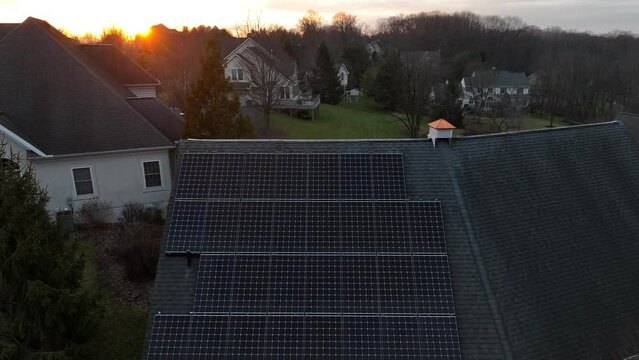 Aerial rising shot of solar panels on sloped roof in luxurious, wealthy neighborhood in America. Winter sunset with solar energy theme.
