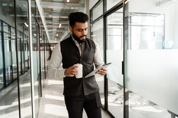 Young indian man in suit using tablet computer in office corridor