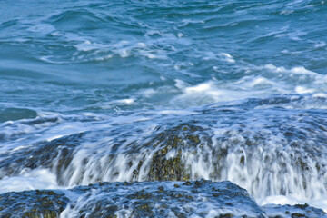 Rocks on the beach, blue water and sea waves.