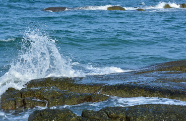 Rocks on the beach, blue water and sea waves.