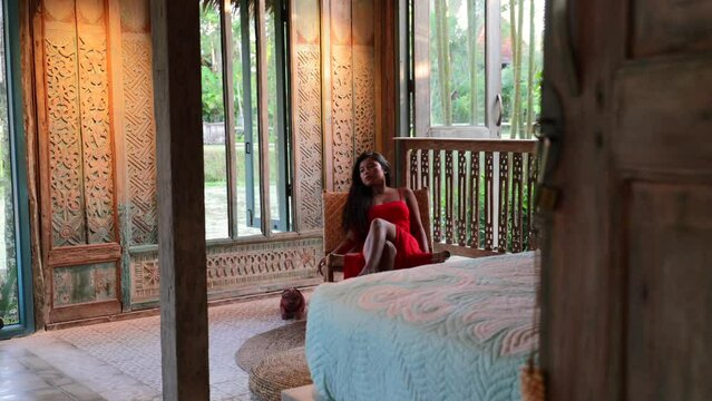 young asian sitting in bohemian bedroom villa with natural garden views outside in bali